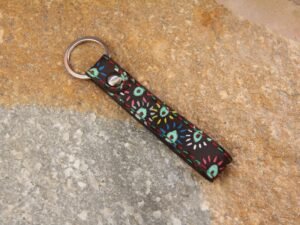 Kleiner Schlüsselanhänger aus dunkelbraunem Leder, bemalt mit bunten Punkten, die Garnfarbe ist in rot und grün