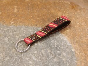 Kleiner Schlüsselanhänger aus Leder in dunkelbraun, bunt bemalt, Garnfarbe in orange und gelb