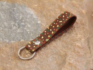 Kleiner Schlüsselanhänger aus Leder in mittelbraun, bemalt mit bunten Punkten, Garnfarbe in grün und orange